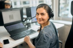 Eine Frau sitzt mit einem Headset vor einem Laptop.