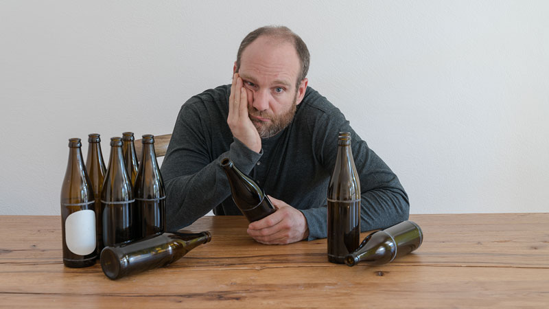 Ein Mann am Tisch mit leergetrunkenen Bierflaschen stützt sich niedergeschlagen auf.