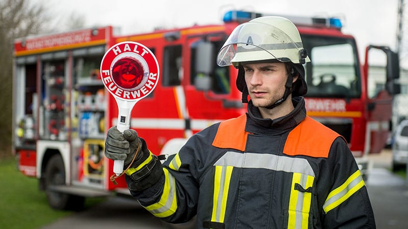 Ein Feuerwehrmann mit Kelle steht vor einem Feuerwehrauto.