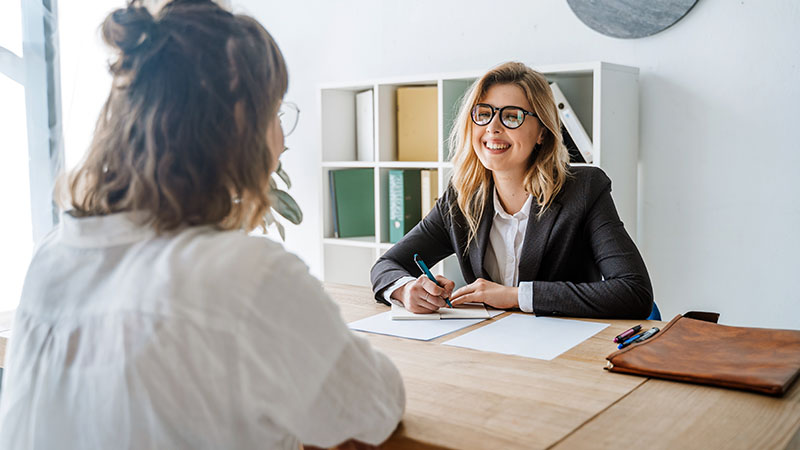 2 Frauen sitzen am Schreibtisch zum Bewerbungsgespräch.