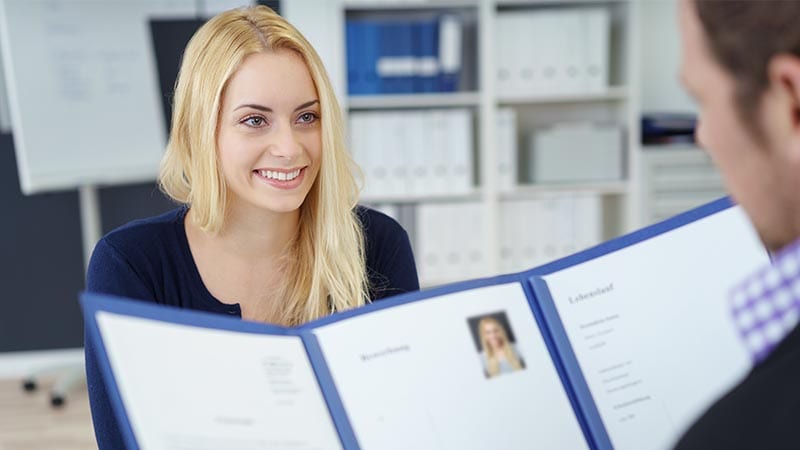 Eine Bewerberin lächelt ihren Gesprächspartner an, der gerade ihre Unterlagen studiert.