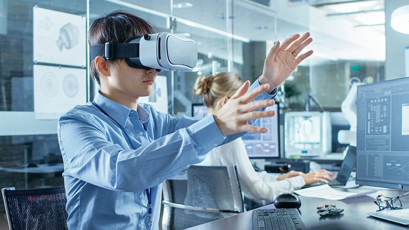 Ein Mann mit VR-Brille sitzt in einem futuristischen Büro und gestikuliert mit den Armen.