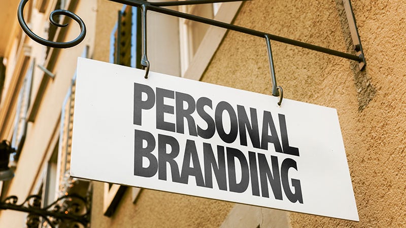 Ein Schild mit "Personal Branding" hängt vor einem Haus.