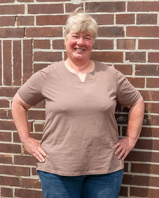 Die stolze Weiterbildungsteilnehmerin Astrid Estel steht, die Hände auf die Hüften gestützt, vor einer geziegelten Hauswand.