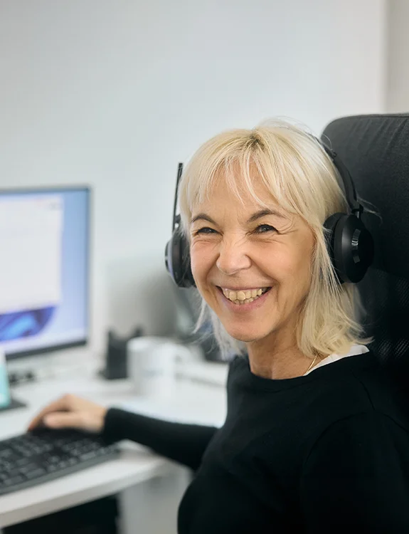 Frau mit Headset sitzt am PC und lächelt