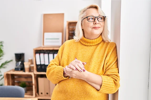 Eine Frau mit Brille lehnt an der Wand und blickt in die Ferne