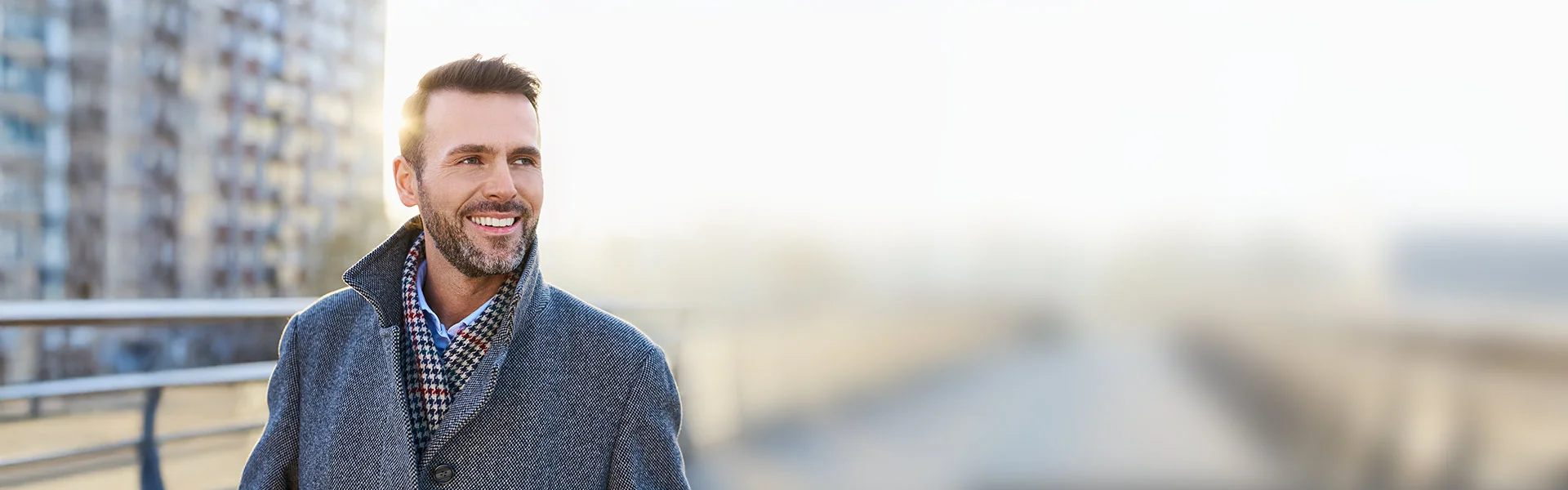 Mann im grauen Mantel steht draußen vor einem Gebäude.