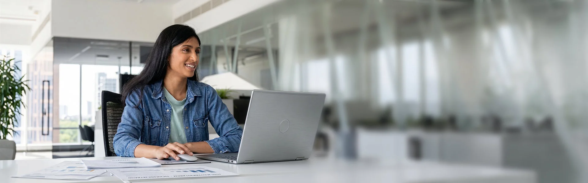 Junge Frau mit braunen langen Haaren sitzt lächelnd vor einem Laptop