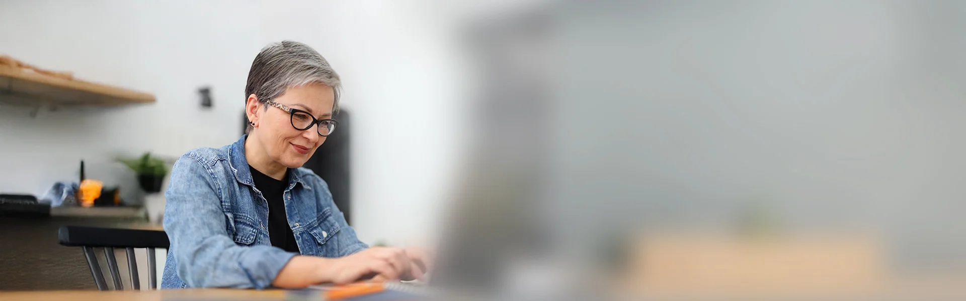 eine Frau sitzt an einem Tisch mit einem Laptop vor orangenem Hintergrund