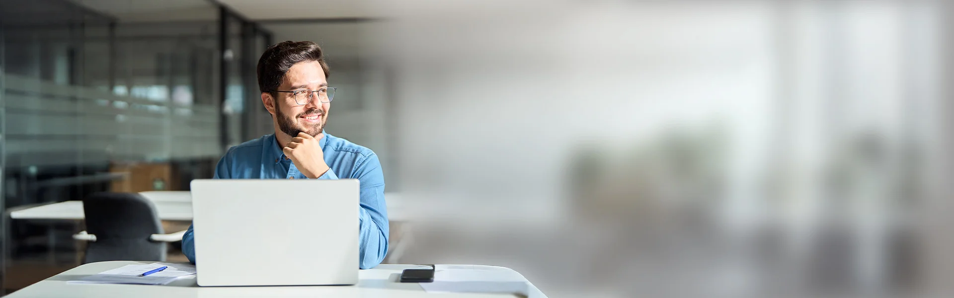 ein Mann sitzt an einem Schreibtisch mit einem Laptop, daneben eine Sprechblase