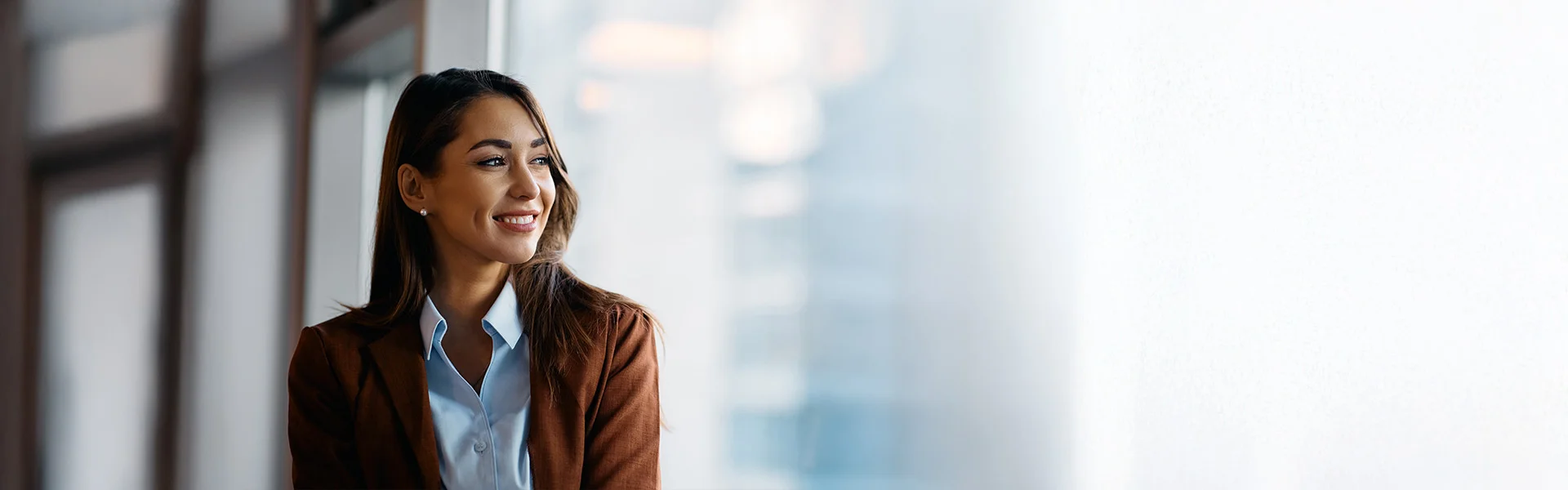 Junge Frau in Bluse und Blazer schaut lächelnd in die Ferne.