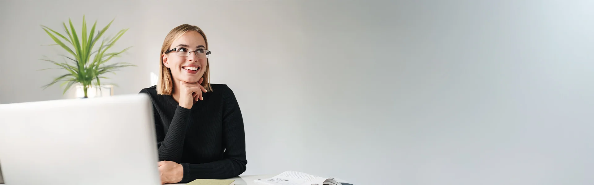 Coachings: Junge Frau sitzt vor einem Laptop und schaut nach ihrem Einzelcoaching glücklich lächelnd zur Seite.