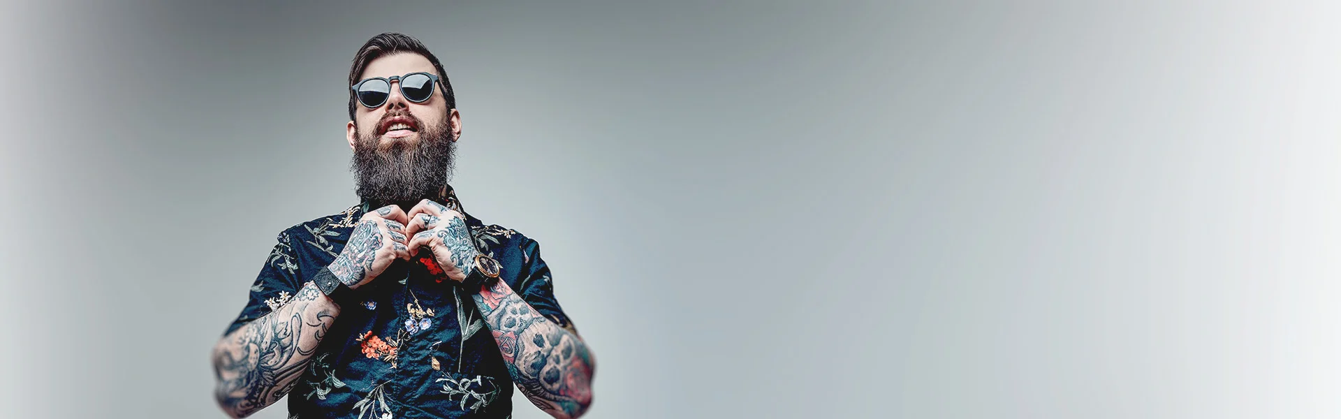Bärtiger Mann mit Sonnenbrille und tätowierten Armen im bunten kurzärmeligen Hemd bereitet sich auf sein Coaching für Personen mit individuellen Anliegen vor.