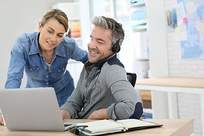 Mann und Frau sitzen lächelnd vor einem Laptop und denken über Förderung für Arbeitnehmer nach