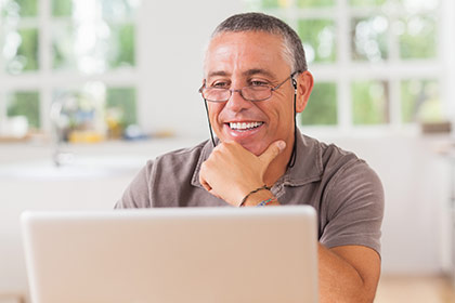 Lächelnder Mann sitzt vor einem Laptop und denkt über eine Weiterbildung für ICDL-Grundlagen nach