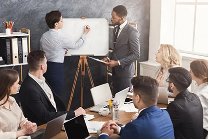 eine Gruppe von Menschen, die um einen Tisch sitzen und zwei Männer die Hände schütteln