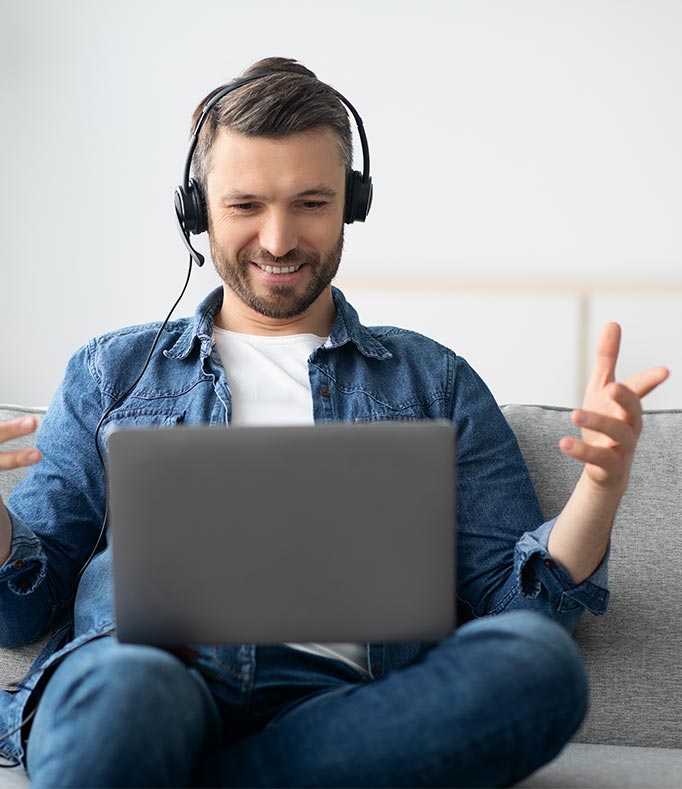 Mann sitzt mit Headset vor einem Laptop und denkt über Probeunterricht für Umschulungen nach