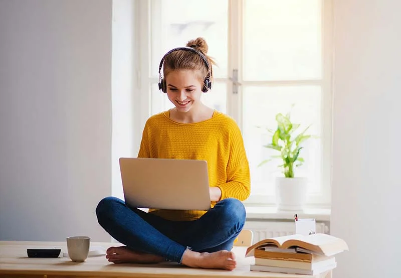 Junge Frau sitzt mit Laptop und Headset auf dem Tisch und lernt.