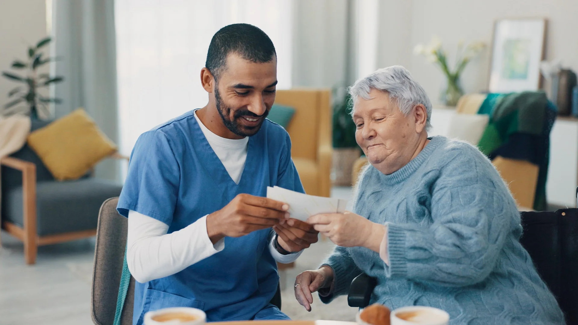 Pfleger sitzt neben alter Dame und schaut sich mit ihr Fotos an.