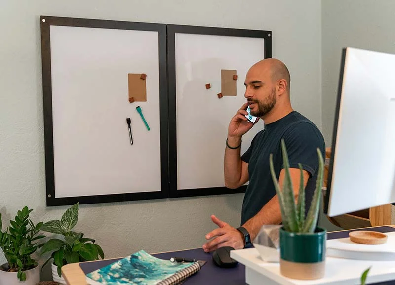 Ein Speditionskaufmann steht telefonierend neben seinem Schreibtisch vor einem Whiteboard.