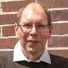 Der erfolgreiche Umschüler André Pardun steht mit verschränkten Armen vor einer geziegelten Hauswand.