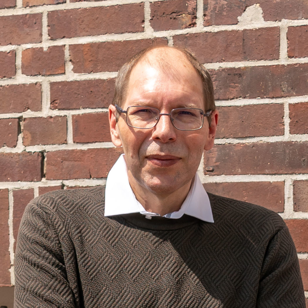 Der erfolgreiche Umschüler André Pardun steht mit verschränkten Armen vor einer geziegelten Hauswand.