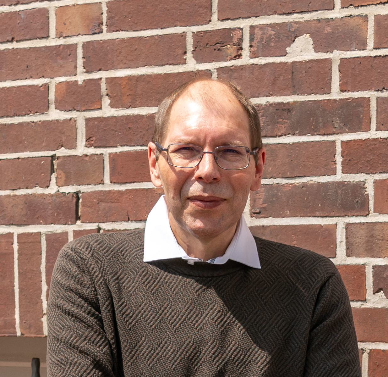 Der erfolgreiche Umschüler André Pardun steht mit verschränkten Armen vor einer geziegelten Hauswand.