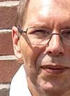 Der erfolgreiche Umschüler André Pardun steht mit verschränkten Armen vor einer geziegelten Hauswand.