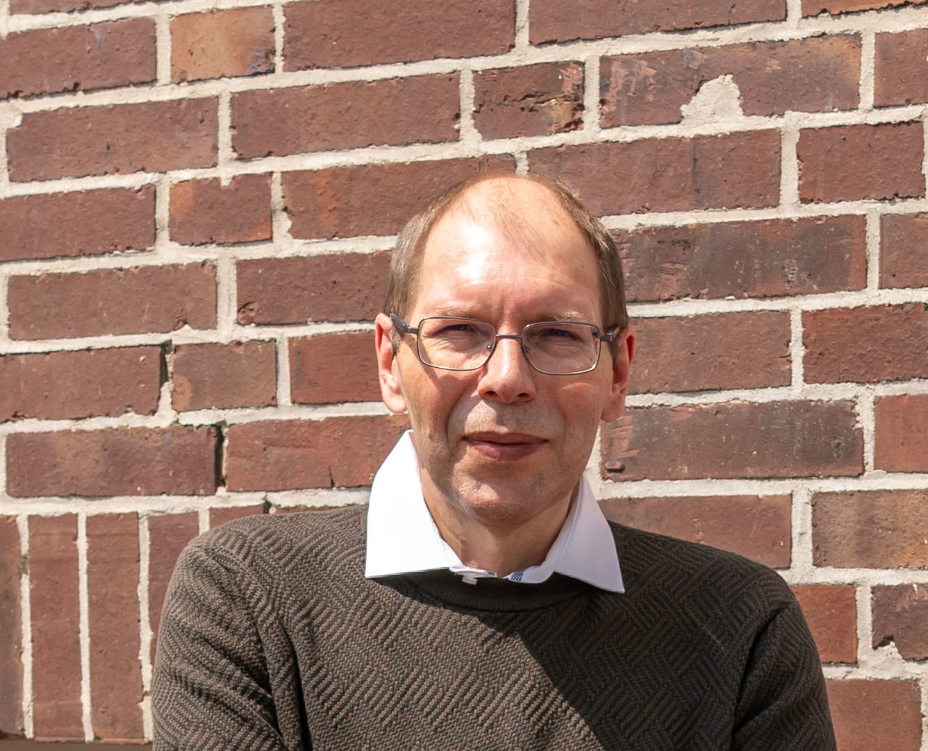 Der erfolgreiche Umschüler André Pardun steht mit verschränkten Armen vor einer geziegelten Hauswand.