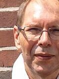 Der erfolgreiche Umschüler André Pardun steht mit verschränkten Armen vor einer geziegelten Hauswand.