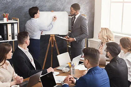 eine Gruppe von Menschen, die um einen Tisch sitzen und zwei Männer die Hände schütteln