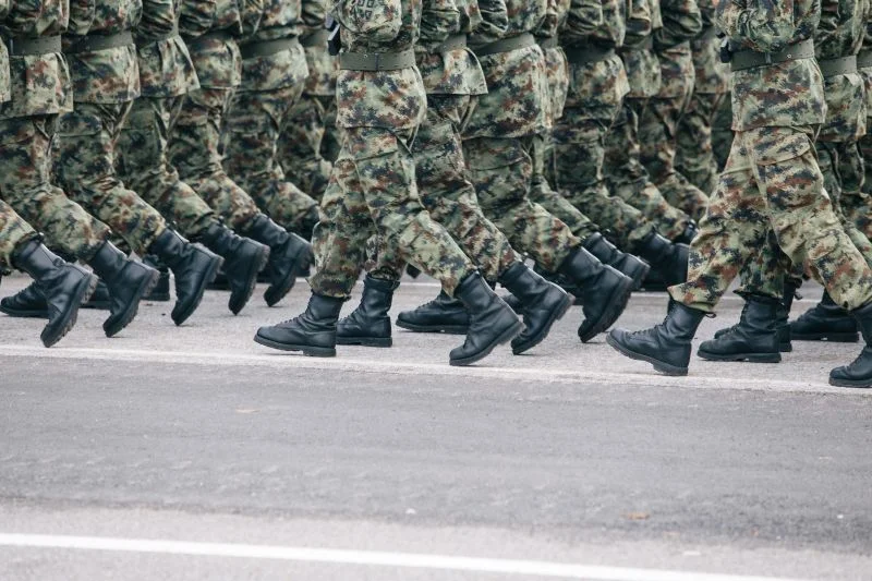Soldatinnen und Soldaten marschieren in Tarnuniform und schwarzen Stiefeln diszipliniert im Gleichschritt (Symbolbild).