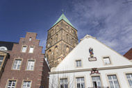 ein großes Gebäude mit einer Uhr auf der Oberseite, davor zwei Wohnhäuser