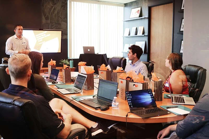 Manager sitzen mit ihren Laptops um einen Konferenztisch und lauschen einem Redner.
