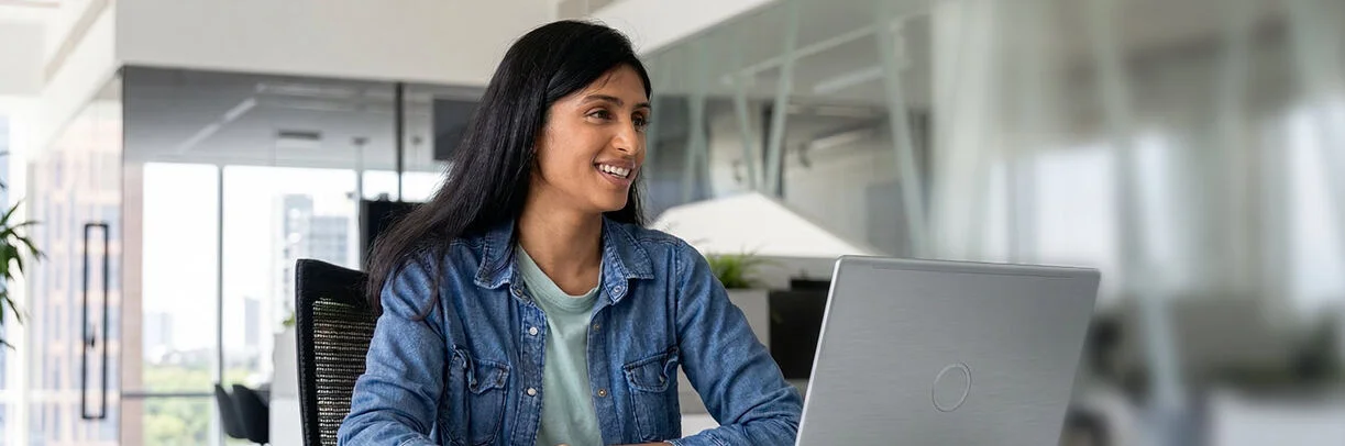 Junge Frau mit braunen langen Haaren sitzt lächelnd vor einem Laptop