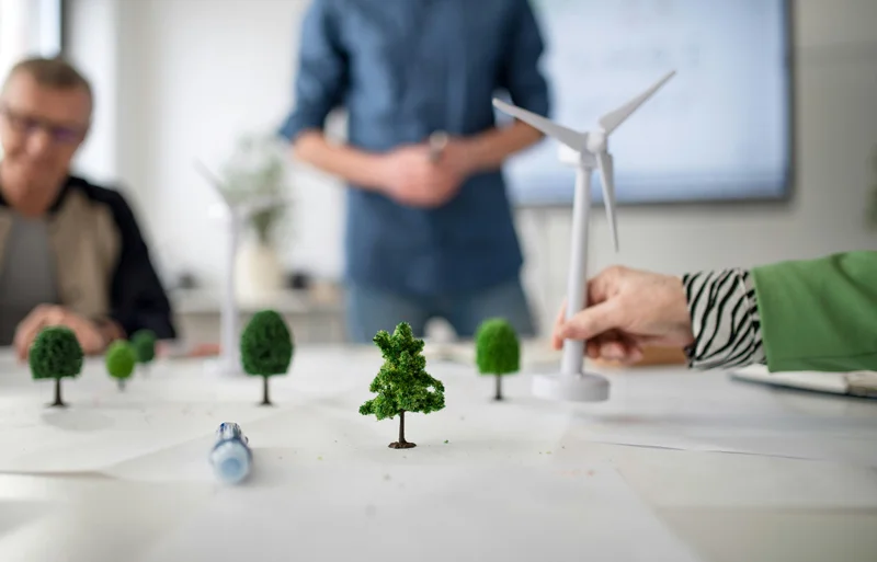 Mehrere Personen um einen Tisch mit Miniaturbäumen und einem Modell‑Windrad – Planung für erneuerbare Energien.