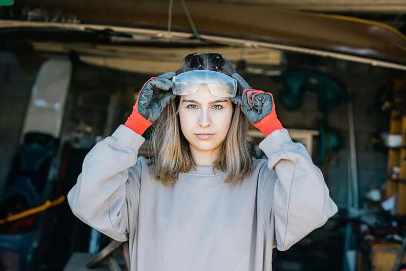 Junge Frau mit Handschuhen setzt eine Schutzbrille auf.