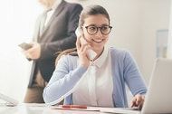 eine Frau sitzt an einem Schreibtisch mit einem Laptop und telefoniert