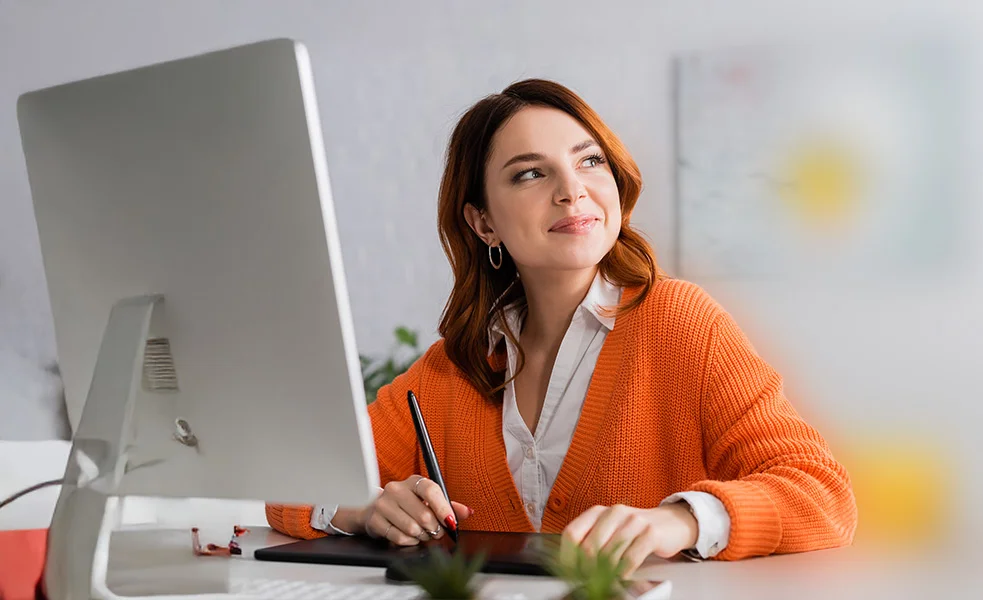 Junge Frau sitzt lächelnd vor einem Computer-Monitor.