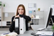 eine Frau, die an einem Schreibtisch mit einem Computer sitzt und sich auf Ordnern abstützt