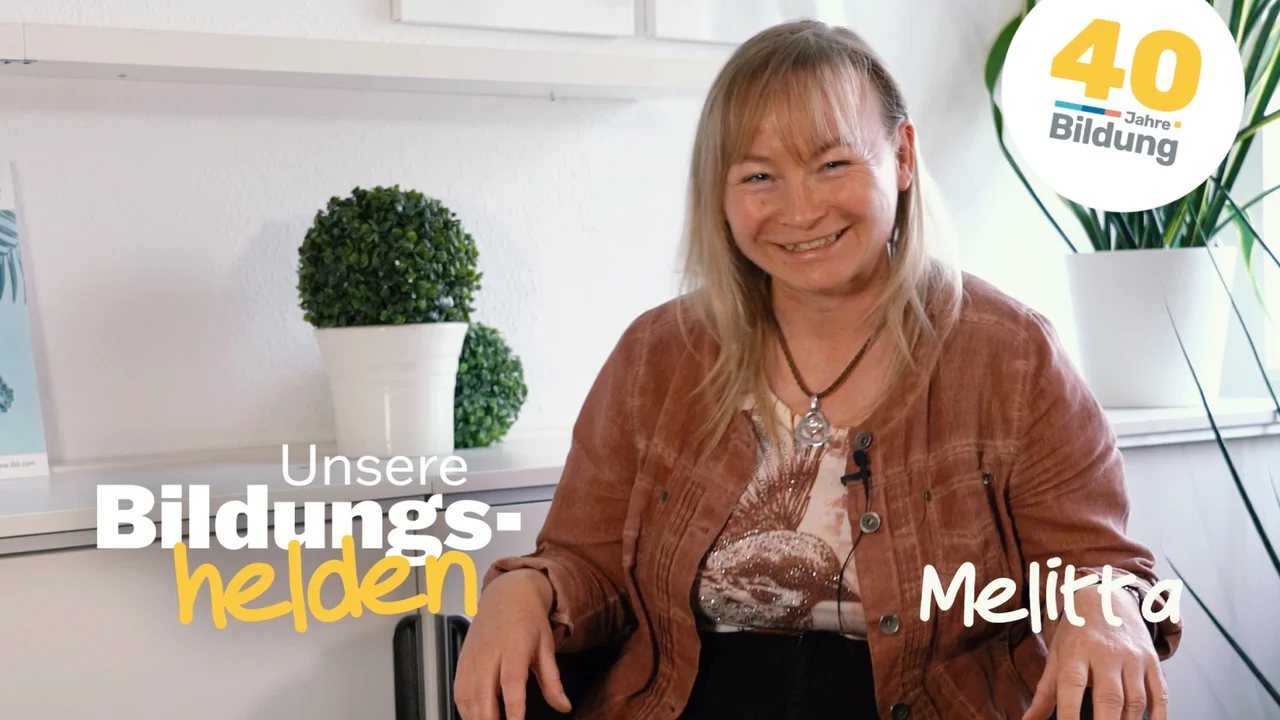 Video-Vorschaubild aus der Reihe "40 Jahre IBB - Bildungshelden": Melitta Vogenauer, IBB-Weiterbildungsteilnehmerin, sitzt glücklich lächelnd in einer bequemen Sitzecke am IBB-Standort in Stendal.