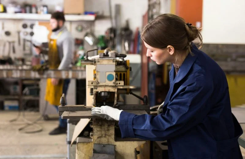 Junge Frau im blauen Overall arbeitet an einer Maschine