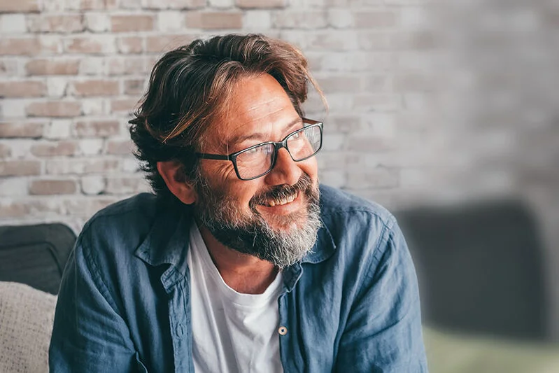Mann sitzt im Wohnzimmer auf einem Sofa, schaut nachdenklich.