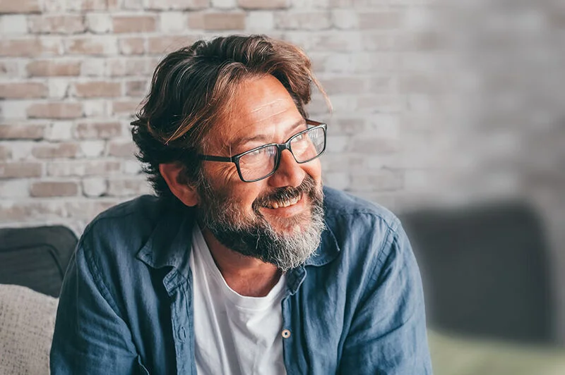 Mann sitzt im Wohnzimmer auf einem Sofa, schaut nachdenklich.