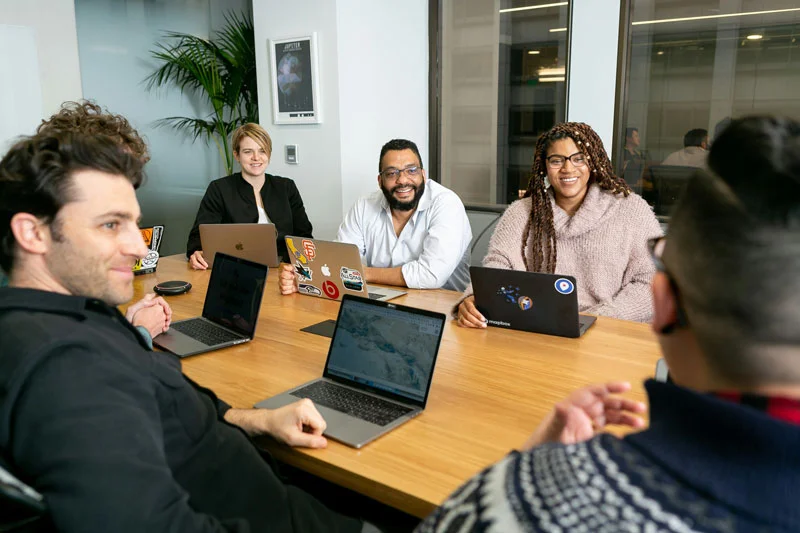 5 Personen mit Laptop an einem Besprechungstisch