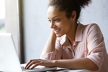 Lächelnde Frau sitzt vor einem Laptop und denkt über eine Weiterbildung für ICDL Textverarbeitungen nach