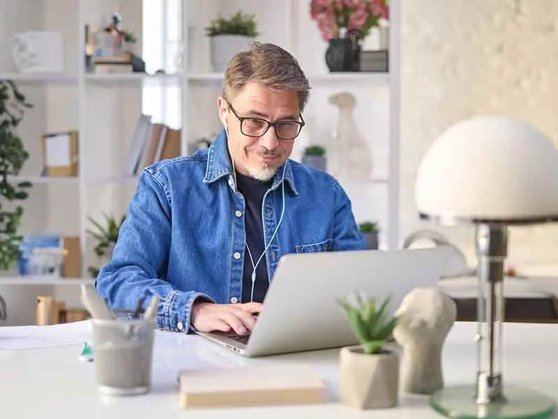 ein Mann in einer blauen Jacke und Brille, der an einem Laptop arbeitet